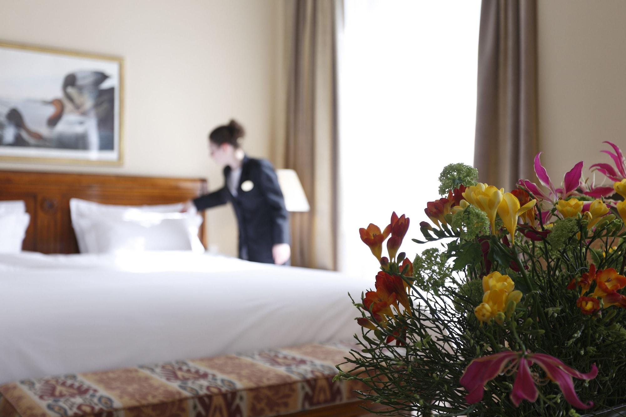 Hotel Le Plaza Bruselas Exterior foto The photo shows a hotel room with a neatly made bed in the background. A staff member, dressed in a uniform, is fixing the bed. In the foreground, there is a bouquet of colorful flowers, adding a touch of vibrancy to the scene. The room is well-lit, 