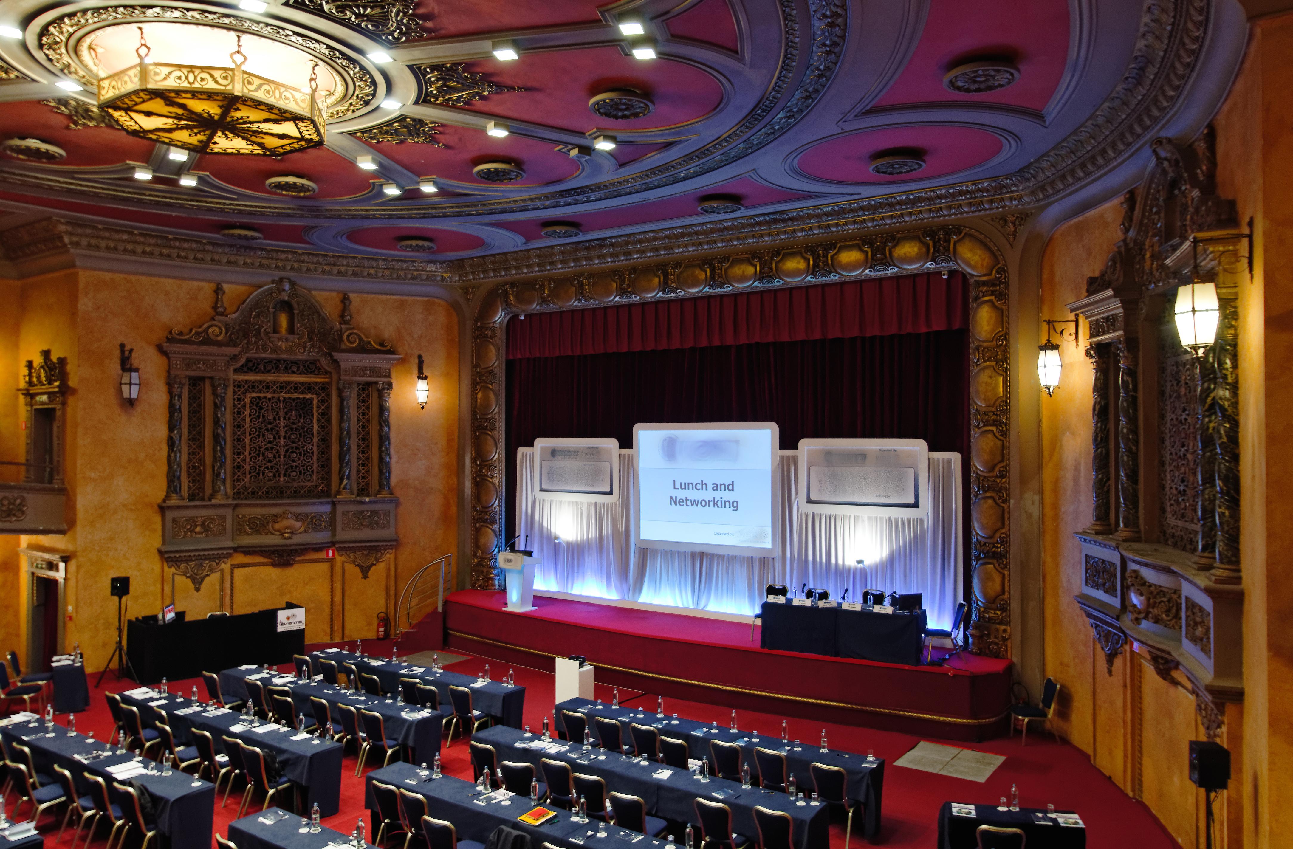 Hotel Le Plaza Bruselas Exterior foto The photo shows a spacious banquet or conference hall with a stage set up for an event. The stage features a large screen with the words "Lunch and Networking" displayed prominently. In front of the stage, there are several rows of neatly arranged ta