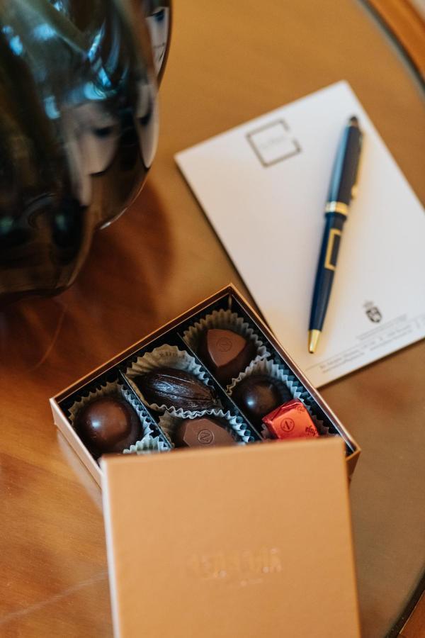 Hotel Le Plaza Bruselas Exterior foto The photo shows a beautifully arranged box of chocolates with various shapes and designs inside. The box is made of cardboard, featuring a clear top that displays the chocolates. The chocolates appear to be a mix of glossy dark chocolate and wrapped 