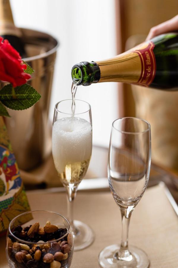 Hotel Le Plaza Bruselas Exterior foto The photo shows a bottle of sparkling wine being poured into a champagne flute. The glass is slowly filling with bubbly liquid, creating a frothy head. Next to the flute, there is an empty glass, and there are some decorative elements in the backgrou