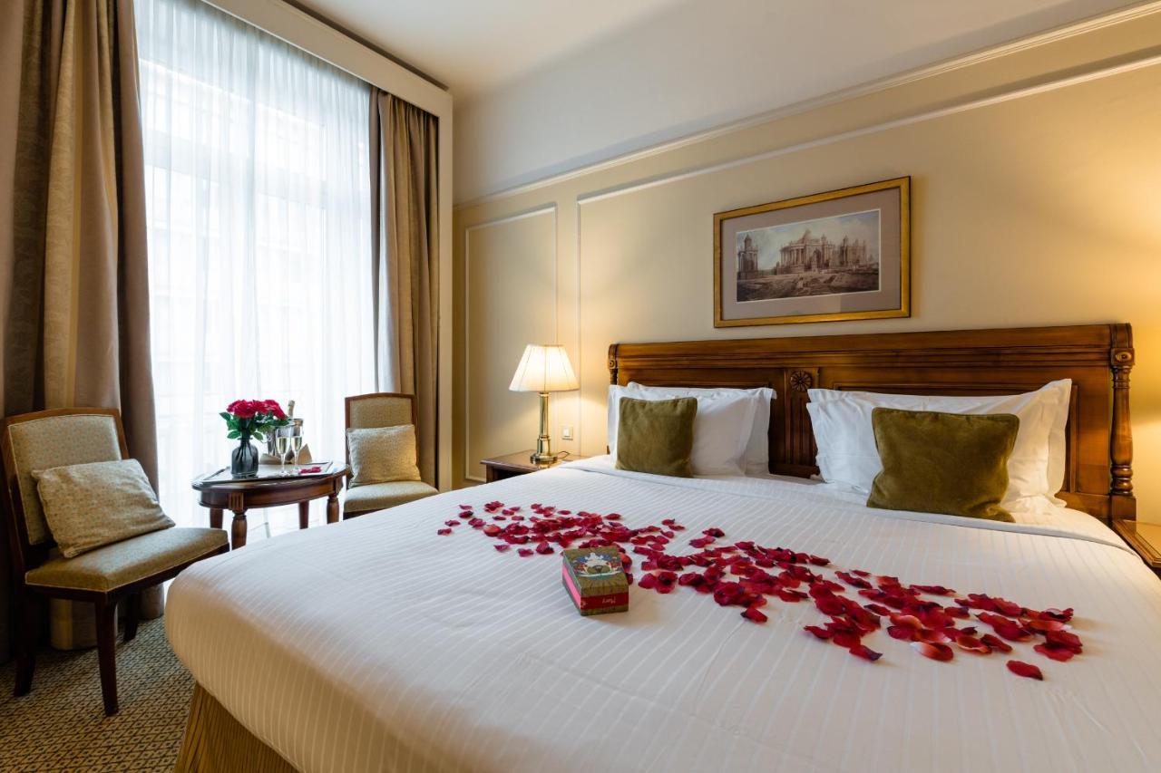 Hotel Le Plaza Bruselas Exterior foto The photo shows a cozy and elegantly designed hotel room. There is a large bed with white linens, adorned with green pillows. Petals from red flowers are scattered across the bed, creating a romantic atmosphere. Beside the bed, there are two chairs a