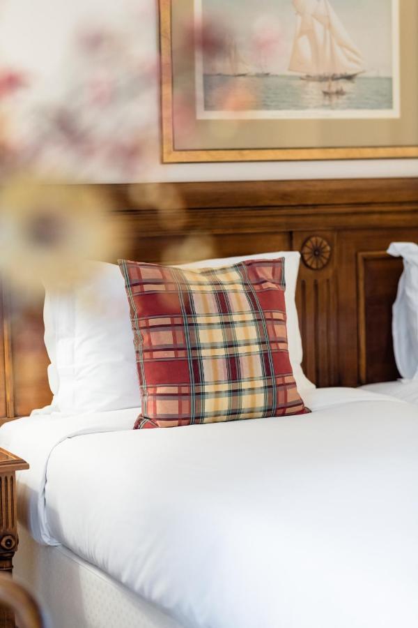 Hotel Le Plaza Bruselas Exterior foto The photo shows a decorative plaid pillow placed on a bed. The pillow features a mix of red, yellow, and dark plaid patterns. The bedding is white, and there is a wooden headboard in the background, which has a decorative design. The overall ambiance