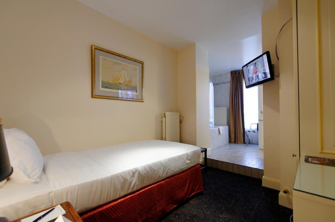 Hotel Le Plaza Bruselas Exterior foto The photo shows a small hotel room featuring a single bed with white linens and a dark red bed skirt. There's a painting on the wall above the bed. A flat-screen television is mounted on the wall across from the bed. To the right, there's a doorway t