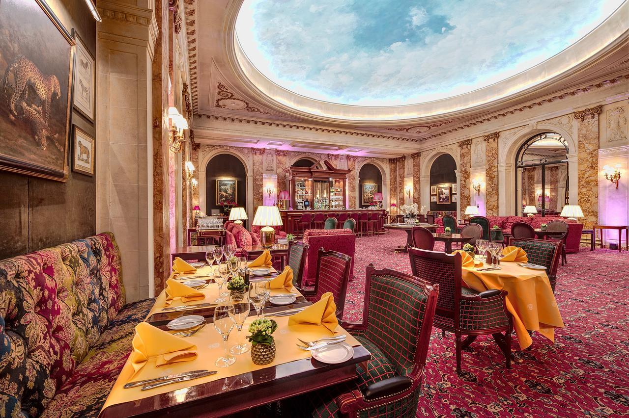 Hotel Le Plaza Bruselas Exterior foto The photo shows an elegant restaurant interior with a luxurious ambiance. The space features a high ceiling with a painted or decorated skylight reminiscent of a clear blue sky. The tables are set neatly with yellow tablecloths, plates, and cutlery, 